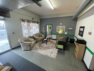 Modern office lounge with gray sofa, green chairs, abstract wall art, and terrazzo flooring under industrial ceiling