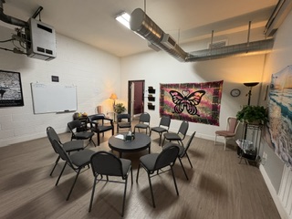 Modern conference room with round black table, gray chairs, exposed ceiling ductwork, and colorful wall art at Vegas Stronger