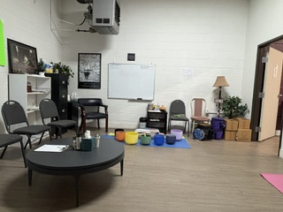 Fitness studio with black folding chairs arranged around coffee table, whiteboard on wall, and colorful exercise equipment on