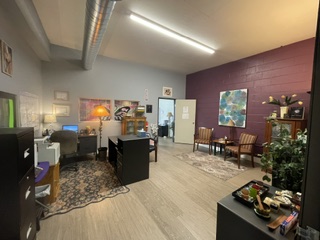 Open office space with modern furniture, area rugs, artwork on burgundy and white walls, and fluorescent lighting