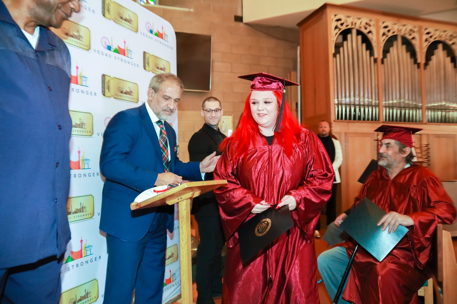Presenter completes paperwork beside graduate with diploma