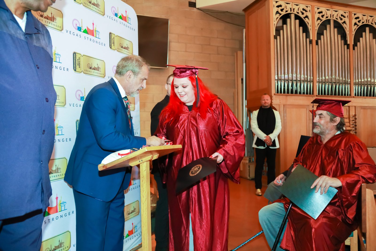 Presenter signs document beside graduate with diploma